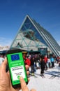 A man on a ski slope near the cable car station and ski lifts holds a smartphone with the European Union digital green pass for