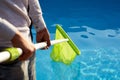 Man with skimmer net equipment cleaning swimming pool from rubbish. Service and maintenance of the pool. Male removes Royalty Free Stock Photo