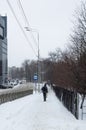 A man with skis walks away on the snowy sidewalk