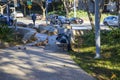 A man sleeping on a bench at Tongva Park with brown fallen leaves and lush green trees, plants and grass with people walking Royalty Free Stock Photo