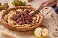 Man slices with silver vintage knife a homemade apple plums pie decorated with fresh apples, plums, grapes, brown raisins Royalty Free Stock Photo