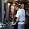 Man slicing meat from gyros rotisserie