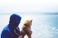 Man with small golden japanese shiba inu dog sitting togetherness on a mountain and looking at blue sea horizon, friends on relax Royalty Free Stock Photo