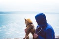 Man with small golden japanese shiba inu dog sitting togetherness on a mountain and looking at blue sea horizon, friends on relax Royalty Free Stock Photo