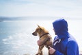 Man with small golden japanese shiba inu dog sitting togetherness on a mountain and looking at blue sea horizon, friends on relax Royalty Free Stock Photo