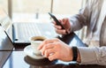 Man in smart watch drinking coffee on work space. Man using laptop, holding smart phone for business work or study. Close up smart