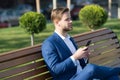Man with smartphone in park. Manager with mobile phone on sunny outdoor. Businessman in blue suit relax on bench. Business lifesty