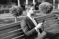 Man with smartphone in park. Manager with mobile phone on sunny outdoor. Businessman in blue suit relax on bench