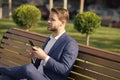 Man with smartphone in park. Manager with mobile phone on sunny outdoor. Businessman in blue suit relax on bench