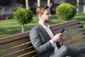 Man with smartphone in park. Manager with mobile phone on sunny outdoor. Businessman in blue suit relax on bench