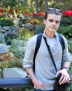 Man smiling with camera bag standing in front of flowers and pond in botanical garden.