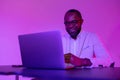 Man smiling at the computer at work. A black programmer works using a laptop computer. the man works at night.