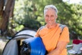 Middle-aged man wearing orange T-shirt carrying blue sleeping bag at campsite by tent and red chair Royalty Free Stock Photo