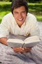 Man smiling while reading a book as he lies on a blanket Royalty Free Stock Photo