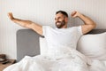 man smiling and stretching arms while sitting up in bed