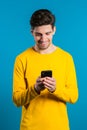 Man sms texting using app on smartphone. Handsome young guy surfing internet with mobile phone. Blue studio background Royalty Free Stock Photo