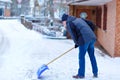 Man with snow shovel cleans sidewalks in winter during snowfall. Winter time in Europe. Young man in warm winter clothes