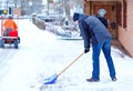 Man with snow shovel cleans sidewalks in winter during snowfall. Winter time in Europe. Young man in warm winter clothes