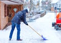 Man with snow shovel cleans sidewalks in winter during snowfall. Winter time in Europe. Young man in warm winter clothes