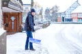 Man with snow shovel cleans sidewalks in winter during snowfall. Winter time in Europe. Young man in warm winter clothes