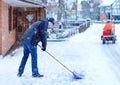 Man with snow shovel cleans sidewalks in winter during snowfall. Winter time in Europe. Young man in warm winter clothes