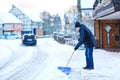 Man with snow shovel cleans sidewalks in winter during snowfall. Winter time in Europe. Young man in warm winter clothes