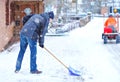 Man with snow shovel cleans sidewalks in winter during snowfall. Winter time in Europe. Young man in warm winter clothes