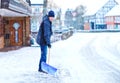 Man with snow shovel cleans sidewalks in winter during snowfall. Winter time in Europe. Young man in warm winter clothes