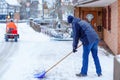 Man with snow shovel cleans sidewalks in winter during snowfall. Winter time in Europe. Young man in warm winter clothes