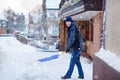 Man with snow shovel cleans sidewalks in winter during snowfall. Winter time in Europe. Young man in warm winter clothes