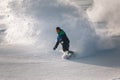 A man snowboarder at speed bends and brakes, splashing loose deep snow