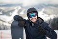 Man snowboarder standing on the top of the snowy slope with snowboard, smiling to the camera, showing thumbs up at winter ski reso Royalty Free Stock Photo