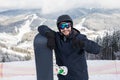 Man snowboarder standing on the top of the snowy slope with snowboard, smiling to the camera, showing thumbs up at winter ski reso Royalty Free Stock Photo