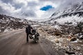 Man solo ridder in ridding gears with loaded motorcycle at isolated road and snow cap mountains