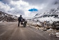 Man solo ridder in ridding gears with loaded motorcycle at isolated road and snow cap mountains