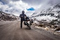 Man solo ridder in ridding gears with loaded motorcycle at isolated road and snow cap mountains