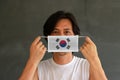 A man with South Korea flag on hygienic mask in his hand and lifted up the front face on dark grey background. Tiny Particle or Royalty Free Stock Photo