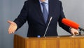 Man speaks in front of microphones, gesturing and standing behind a podium or pulpit. Lawyer, politician, businessman or teacher. Royalty Free Stock Photo