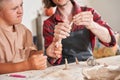 Man with special needs working with clay in ceramic studio under supervision of craftsman