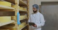 Man specialist in white uniform checking cheeses quality working at producing farm. Male farmer at own dairy factory. Royalty Free Stock Photo