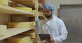 Man specialist in white uniform checking cheeses quality working at producing farm. Male farmer at own dairy factory. Royalty Free Stock Photo