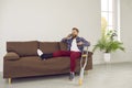 Happy man with broken leg talking to someone on phone while sitting on couch at home Royalty Free Stock Photo