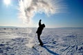 A man splashes boiling water from a mug in the cold on the banks of a frozen river against the background of the morning sun. Royalty Free Stock Photo