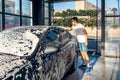 A man is sponging foam on his car at a self-service car wash station