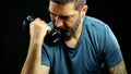 Man in sportswear doing biceps curls with 3kg dumbbells, workout on black background. Royalty Free Stock Photo