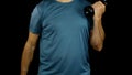 Man in sportswear doing biceps curls with 3kg dumbbells, workout on black background. No face.