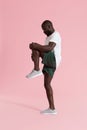 Man in sportswear stretching legs, warming up on pink background