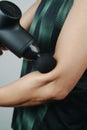 Man in sportwear uses a massage gun on his arm