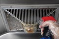 A man spraying chemical liquid to an oily filter hood of a kitchen ventilator at horizontal composition