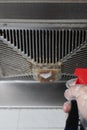 A man spraying chemical liquid to an oily filter hood of a kitchen ventilator at vertical composition